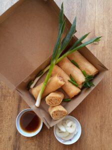 Crispy eggrolls with green onions in a paper to-go container