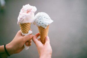 Hands holding two sugar cones with scoops of strawberry and pistachio ice cream