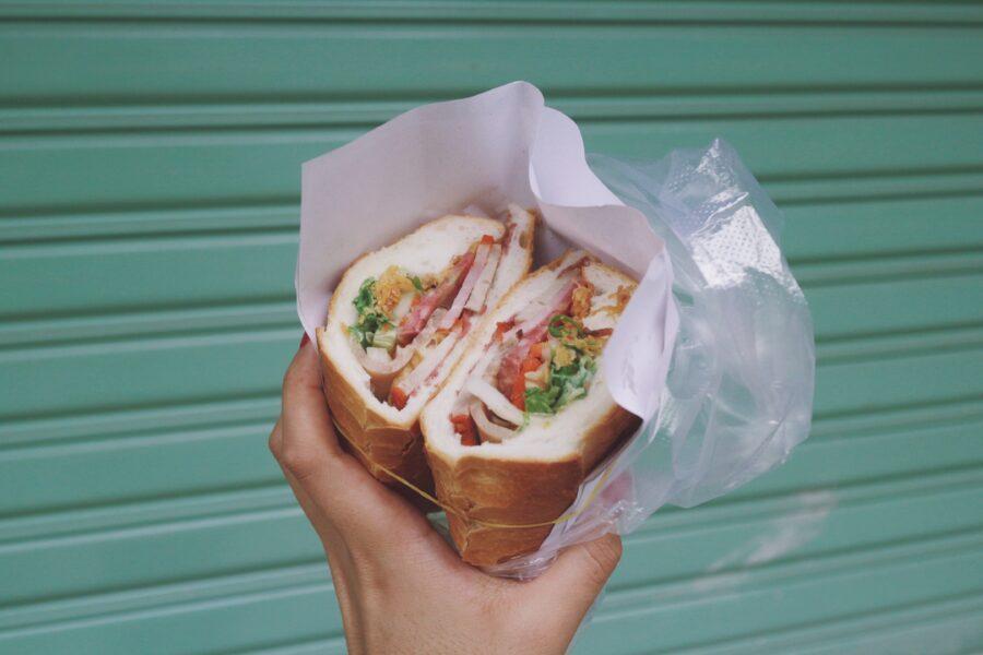 Hand holding a halved deli sandwich wrapped in paper