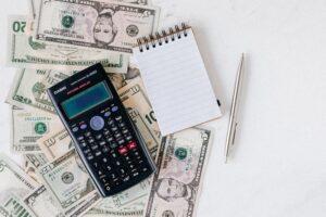 A small pile of cash under a calculator and notepad