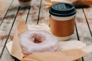 To-go glazed donut and coffee on a picnic table