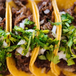 Line of carnitas tacos garnished with cilantro and onion